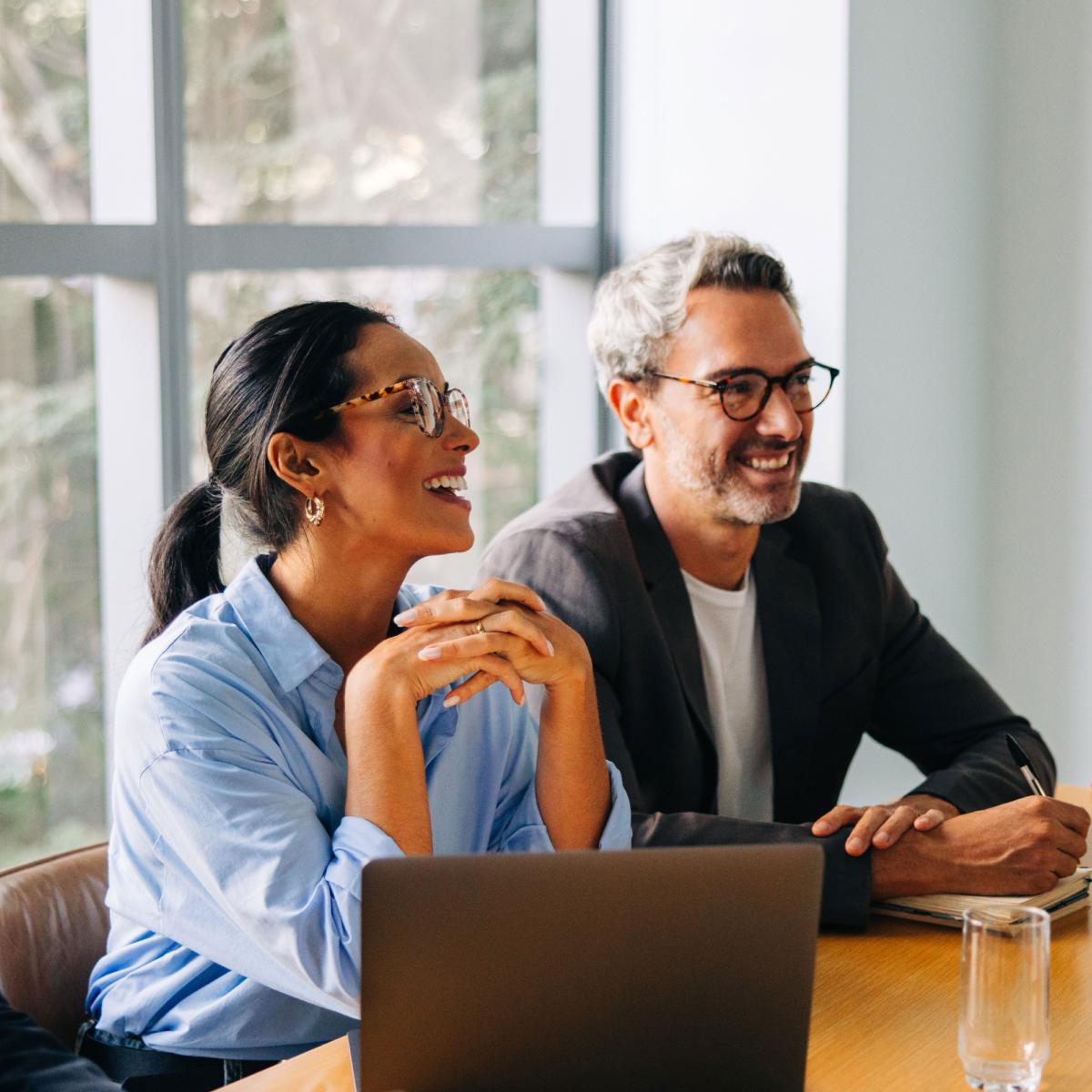 Two colleagues smiling while working on a laptop