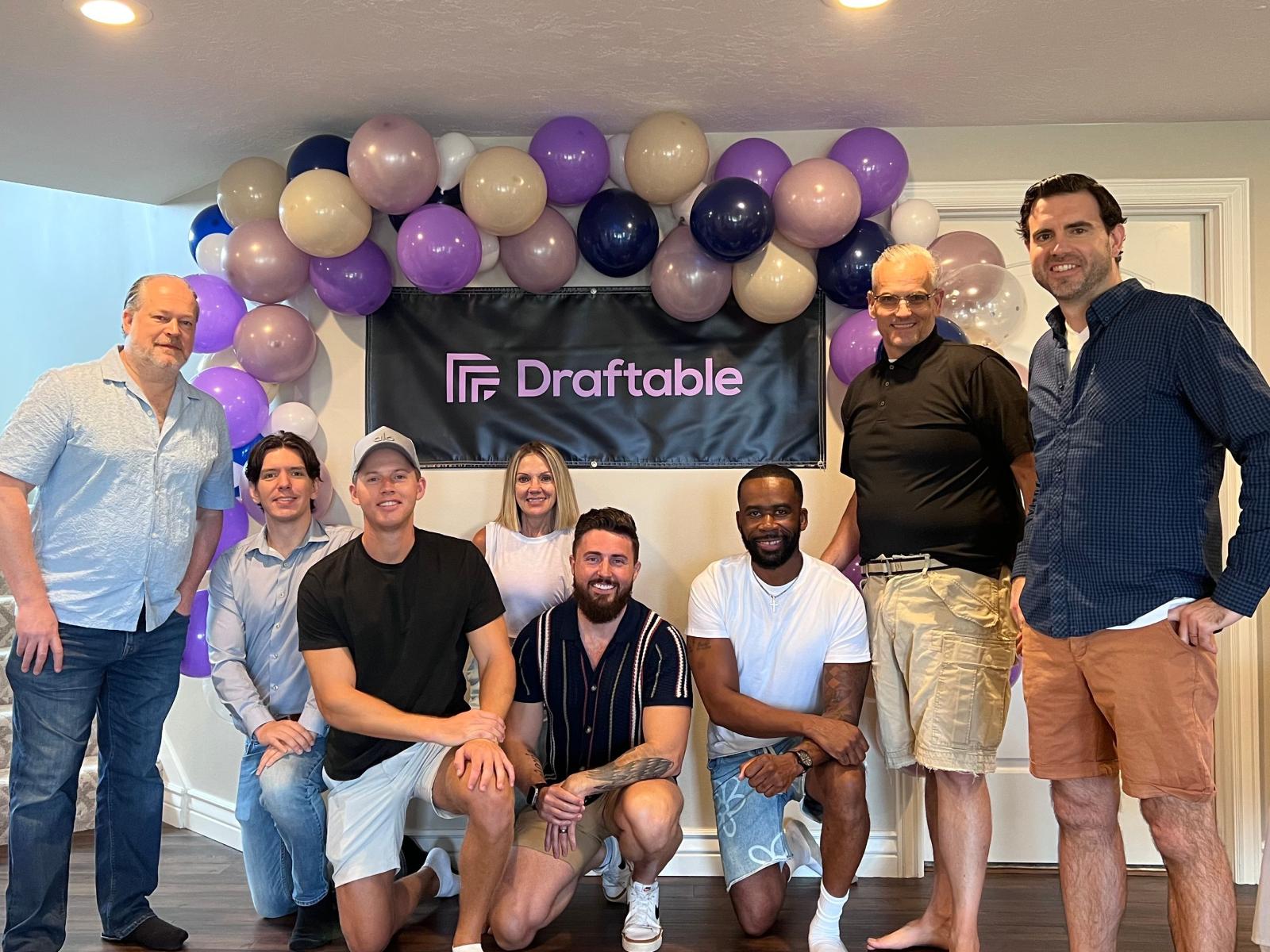 Draftable team gathered in front of a branded backdrop with balloons