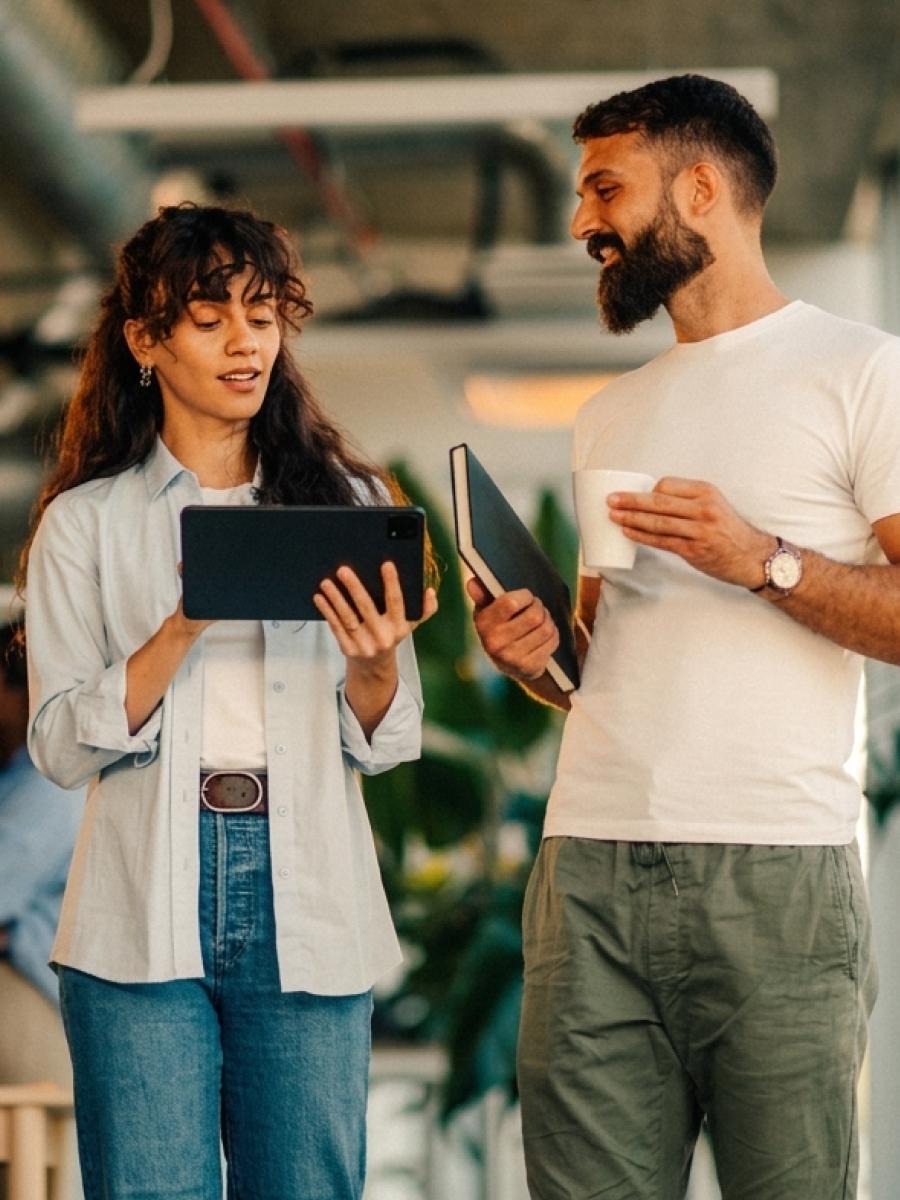 Two colleagues talking in an office, one holding a tablet